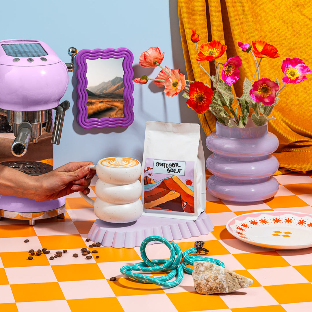 Colorful coffee setup with a coffee machine, coffee beans, and decorative elements on a checkered tablecloth. Coffee is caramel dunes which is our bestselling blend
