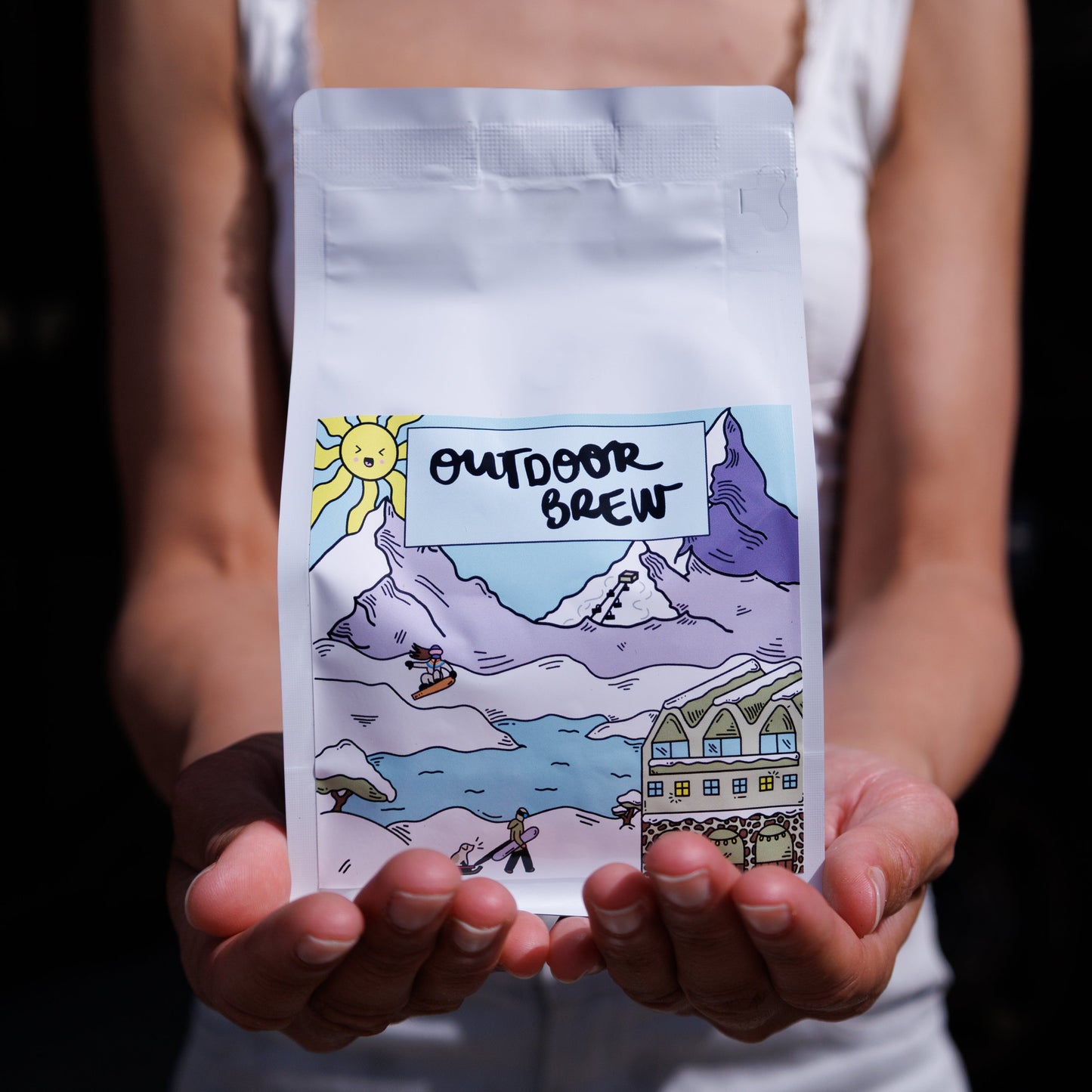 Person holding a coffee bag with 'Outdoor Brew' branding and a snowy mountain design. Coffee is single origin colombian.